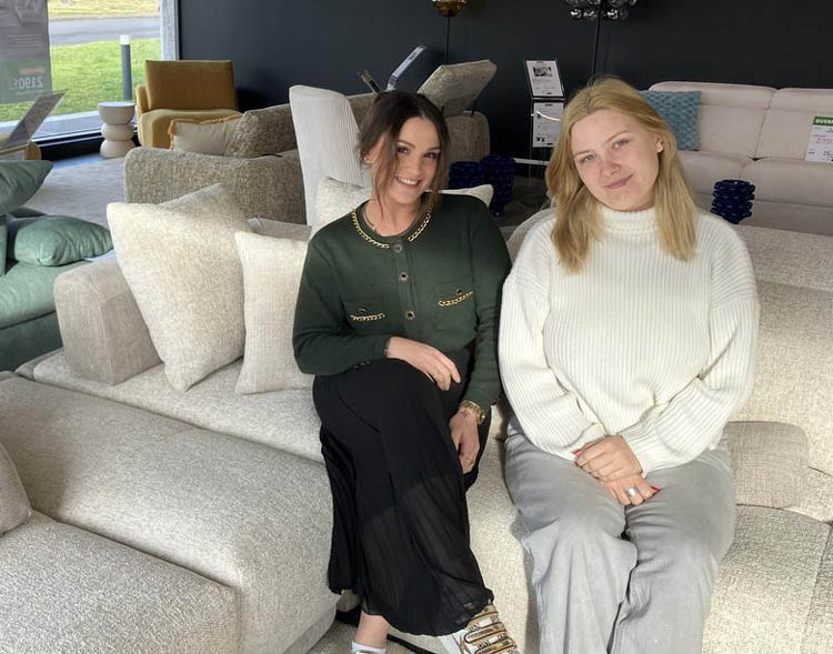 Deux personnes souriantes sont assises sur un canap dans un salon moderne avec des meubles confortables et une grande fen tre laissant entrer la lumi re naturelle.  Description g n r e par IA