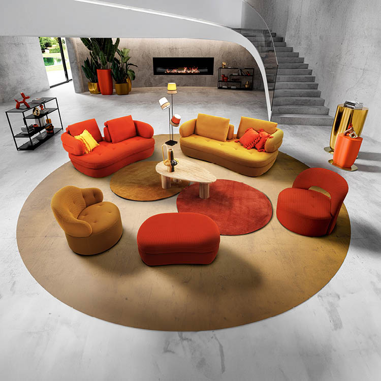 Un salon moderne avec un canap orange et un canap  jaune, deux fauteuils et un pouf assortis, une table basse en bois clair, des tapis ronds orange et rouge, une chemin e encastr e et un escalier en b ton dans un espace lumineux et  pur .  Description g n r e par IA
