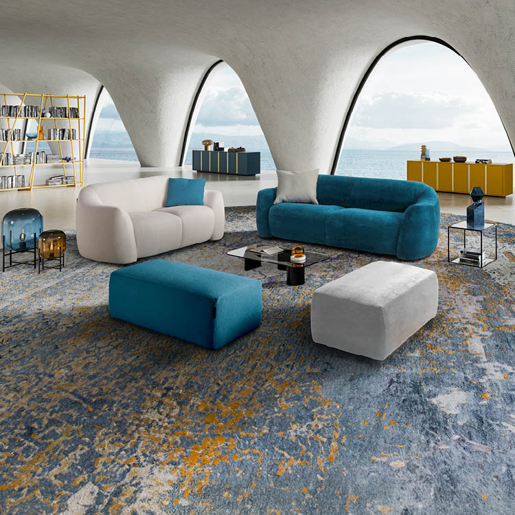 Un salon moderne avec deux canap s arrondis bleu et beige, deux poufs assortis, une table basse noire, un grand tapis color et une biblioth que jaune devant de grandes fen tres en arc donnant sur la mer.  Description g n r e par IA