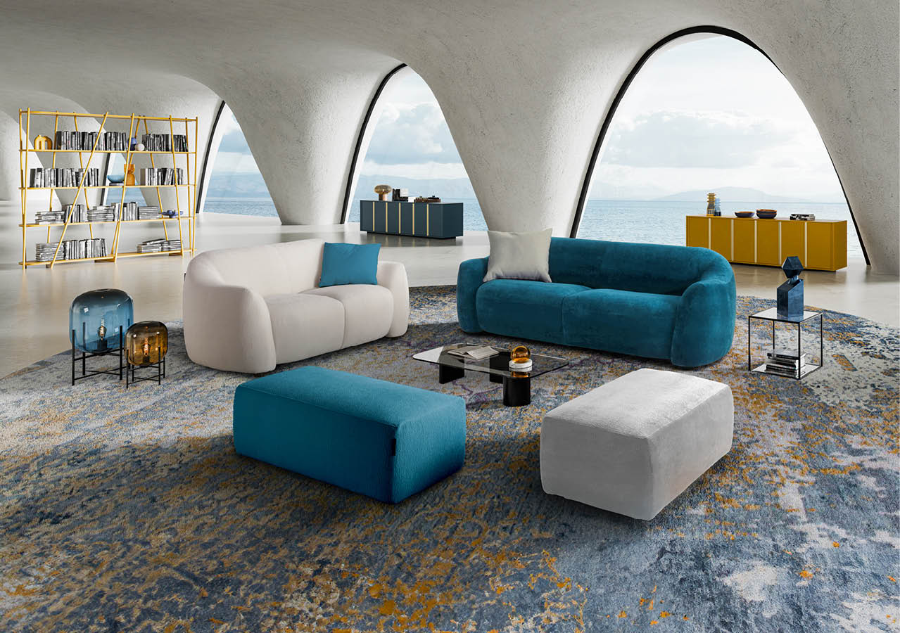 Un salon moderne avec un canap bleu, un canap  blanc, deux poufs, une grande biblioth que jaune, des tables basses en verre et une vue sur la mer   travers de grandes fen tres en arc.  Description g n r e par IA
