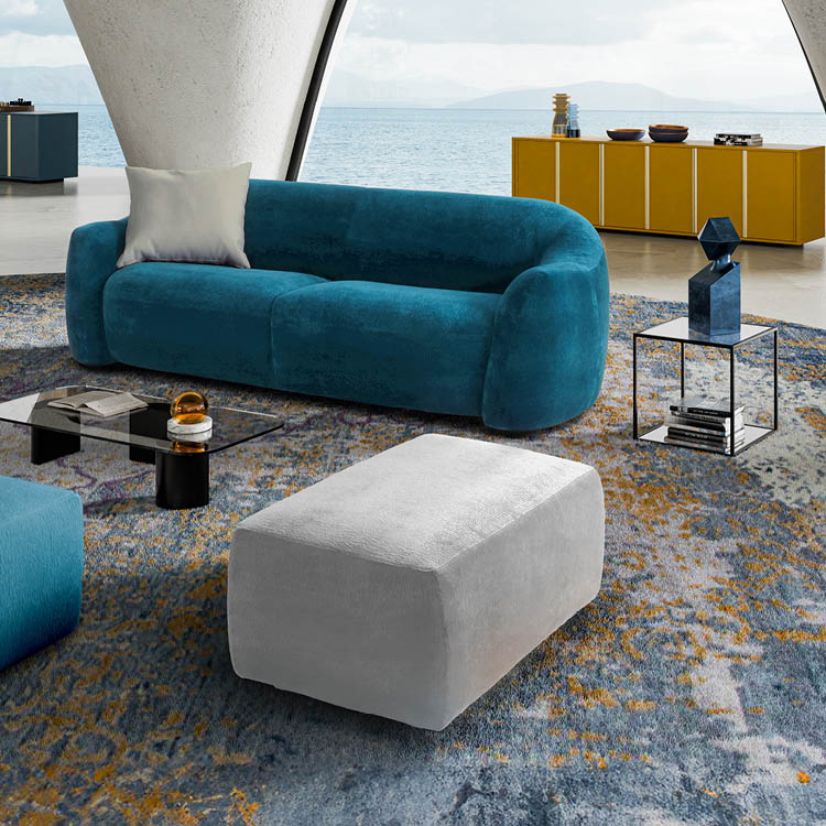 Un salon moderne avec un canap bleu, un pouf gris, une table basse en verre, un tapis color  et une grande baie vitr e donnant sur la mer.  Description g n r e par IA