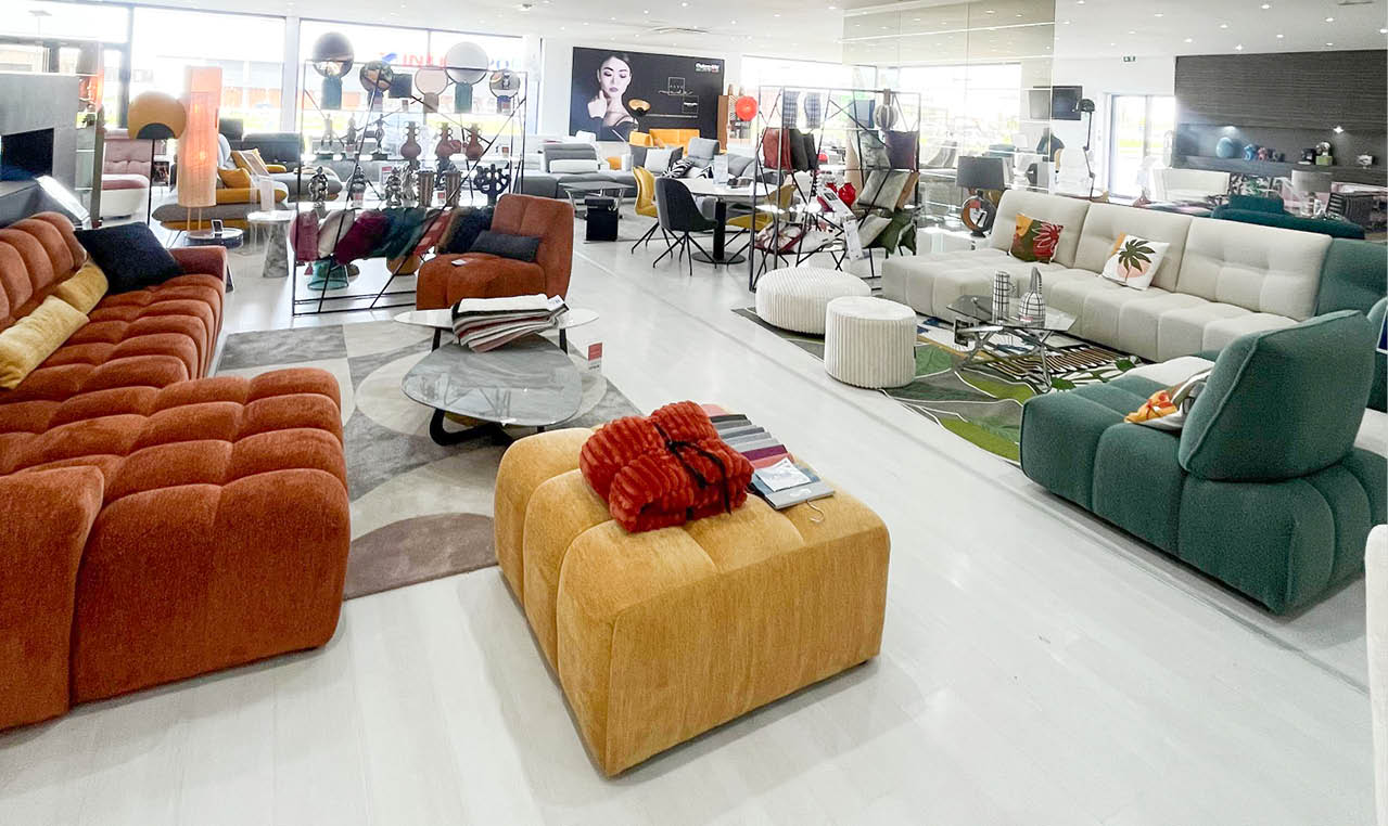 Un grand showroom lumineux pr sente plusieurs canap s modernes et color s dispos s autour de tables basses avec des coussins d coratifs et des accessoires. Description g n r e par IA