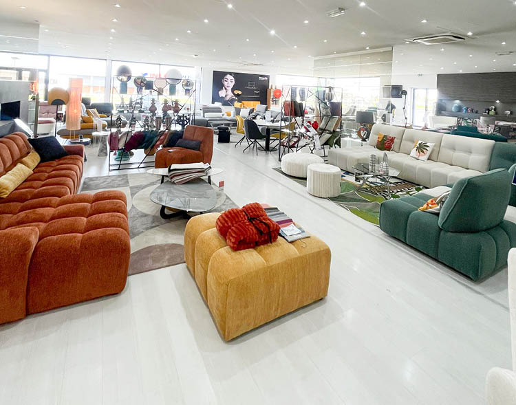 Un grand showroom lumineux pr sente plusieurs canap s modernes et color s dispos s autour de tables basses avec des coussins d coratifs et des tapis. Description g n r e par IA