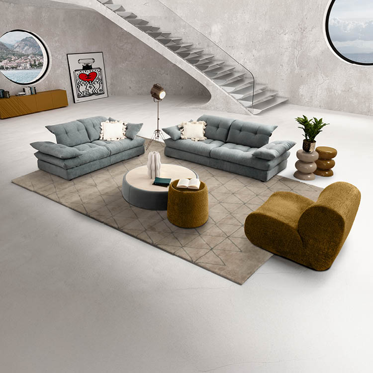 Un salon moderne avec deux canap s gris, un fauteuil beige, une table basse ronde, un tapis beige, une plante en pot, une lampe sur tr pied, un escalier flottant et deux fen tres rondes offrant une vue sur un paysage montagneux. Description g n r e par IA
