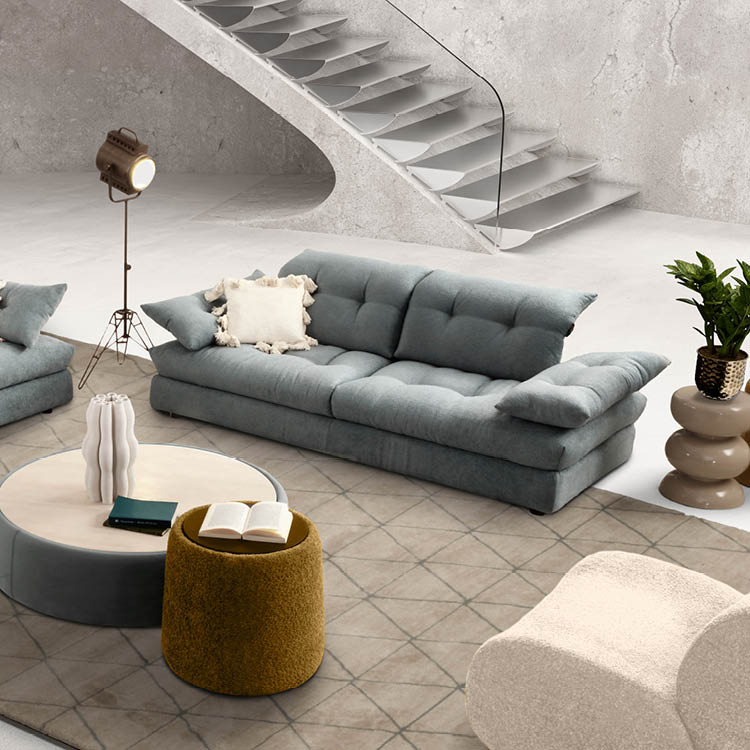 Un salon moderne avec un canap gris, un fauteuil beige, une table basse ronde avec des livres, une lampe sur pied et une plante d corative pr s d'un escalier en b ton.  Description g n r e par IA