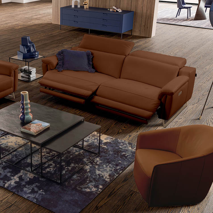 Un salon moderne avec un canap en cuir marron  quip  de repose-pieds relev s, un fauteuil assorti, une table basse noire avec des livres et un vase, et un meuble bas bleu contre un mur en bois.  Description g n r e par IA