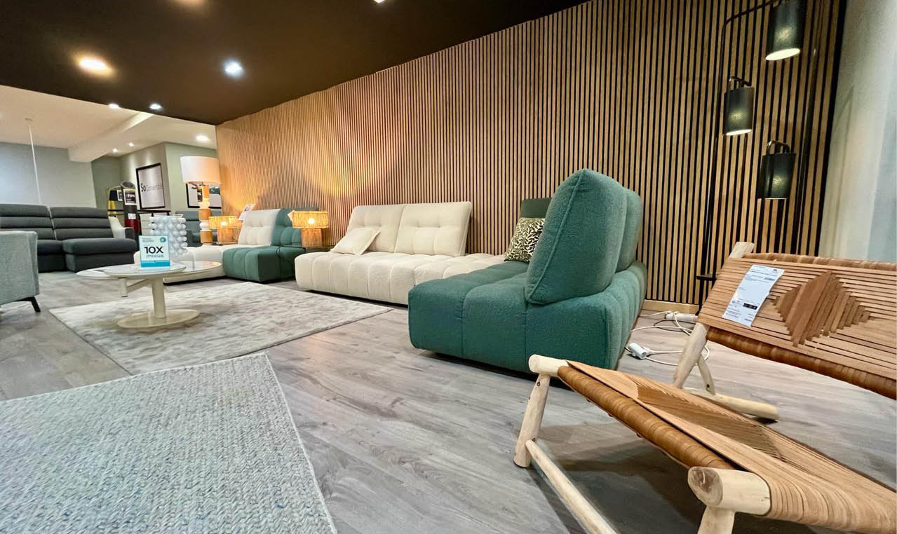 Un salon moderne avec plusieurs canap s et fauteuils color s dispos s sur un sol en bois clair avec un mur en bois  l'arri re-plan et un  clairage suspendu.  Description g n r e par IA