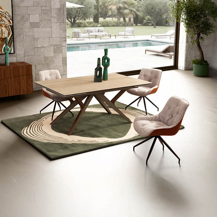 Une salle  manger moderne avec une table en bois clair entour e de quatre chaises rembourr es sur un tapis vert et beige avec une grande baie vitr e donnant sur une piscine et un jardin.  Description g n r e par IA
