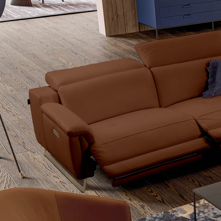 Un canap en cuir marron avec un repose-pieds relev  est plac  dans un salon au sol en bois clair avec un tapis partiellement visible et un meuble bleu en arri re-plan.  Description g n r e par IA