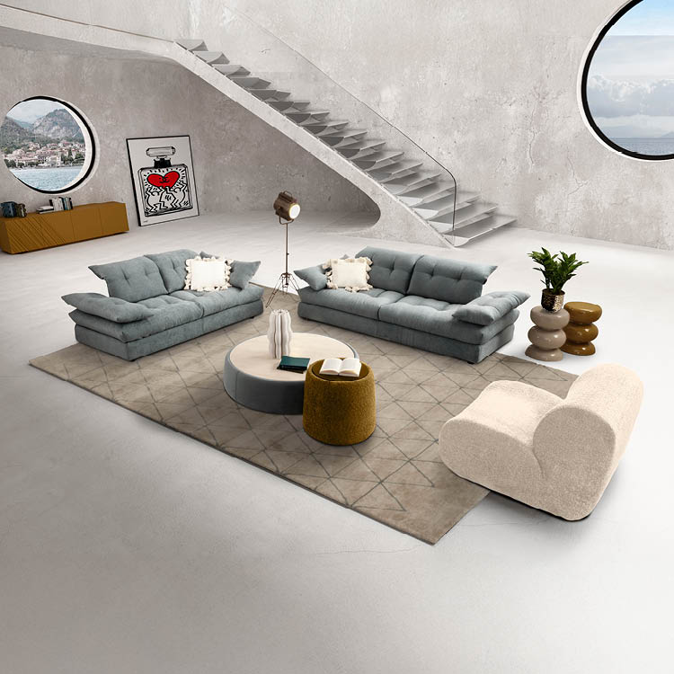 Un salon moderne avec deux canap s gris, un fauteuil beige, une table basse ronde, un tapis beige, une plante en pot, une lampe sur tr pied, un escalier flottant et deux fen tres rondes offrant une vue sur un paysage montagneux. Description g n r e par IA