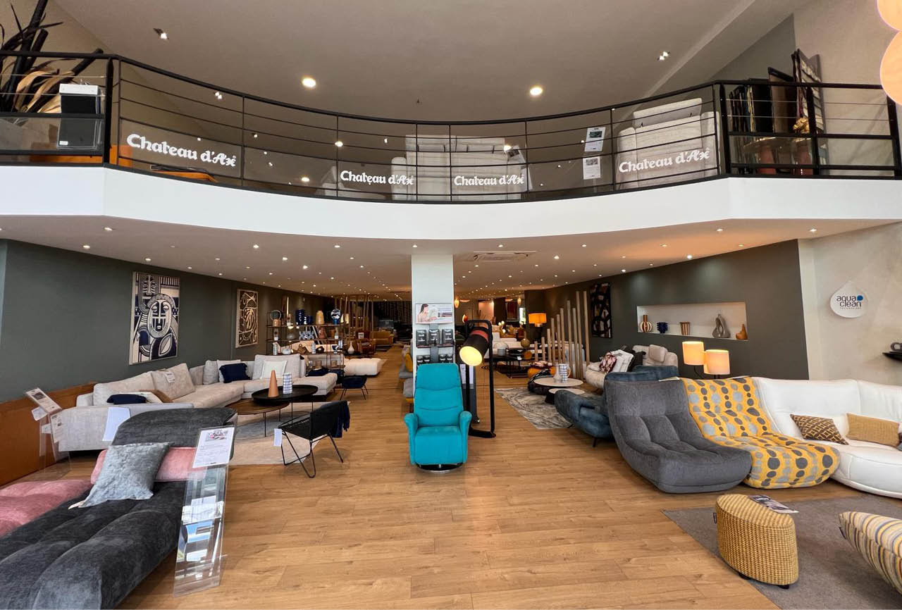 Un magasin de meubles moderne avec plusieurs canap s, fauteuils et poufs dispos s sur un sol en bois clair sous un plafond avec des luminaires encastr s. Description g n r e par IA