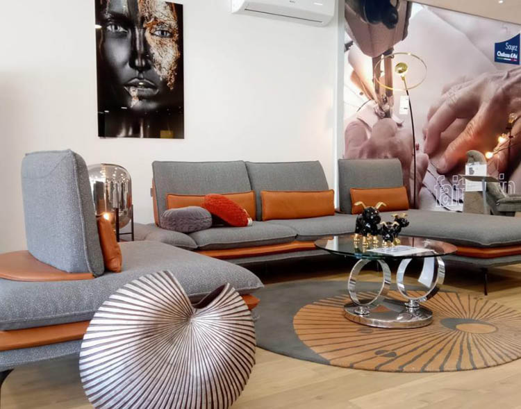 Salon moderne avec canap gris et orange, table basse en verre avec d coration, tapis rond et grande affiche murale montrant une personne effectuant un soin.  Description g n r e par IA