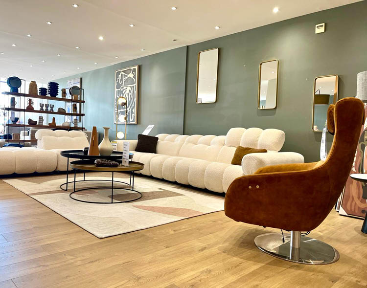 Un salon moderne avec un canap blanc moelleux, une chaise en velours marron, une table basse ronde et des  tag res d coratives contre un mur gris.  Description g n r e par IA