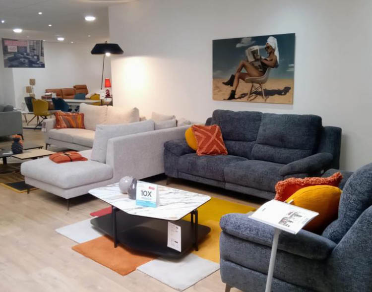 Un salon moderne avec plusieurs canap s et fauteuils color s dispos s autour d'une table basse avec un tapis multicolore et un tableau accroch au mur.  Description g n r e par IA